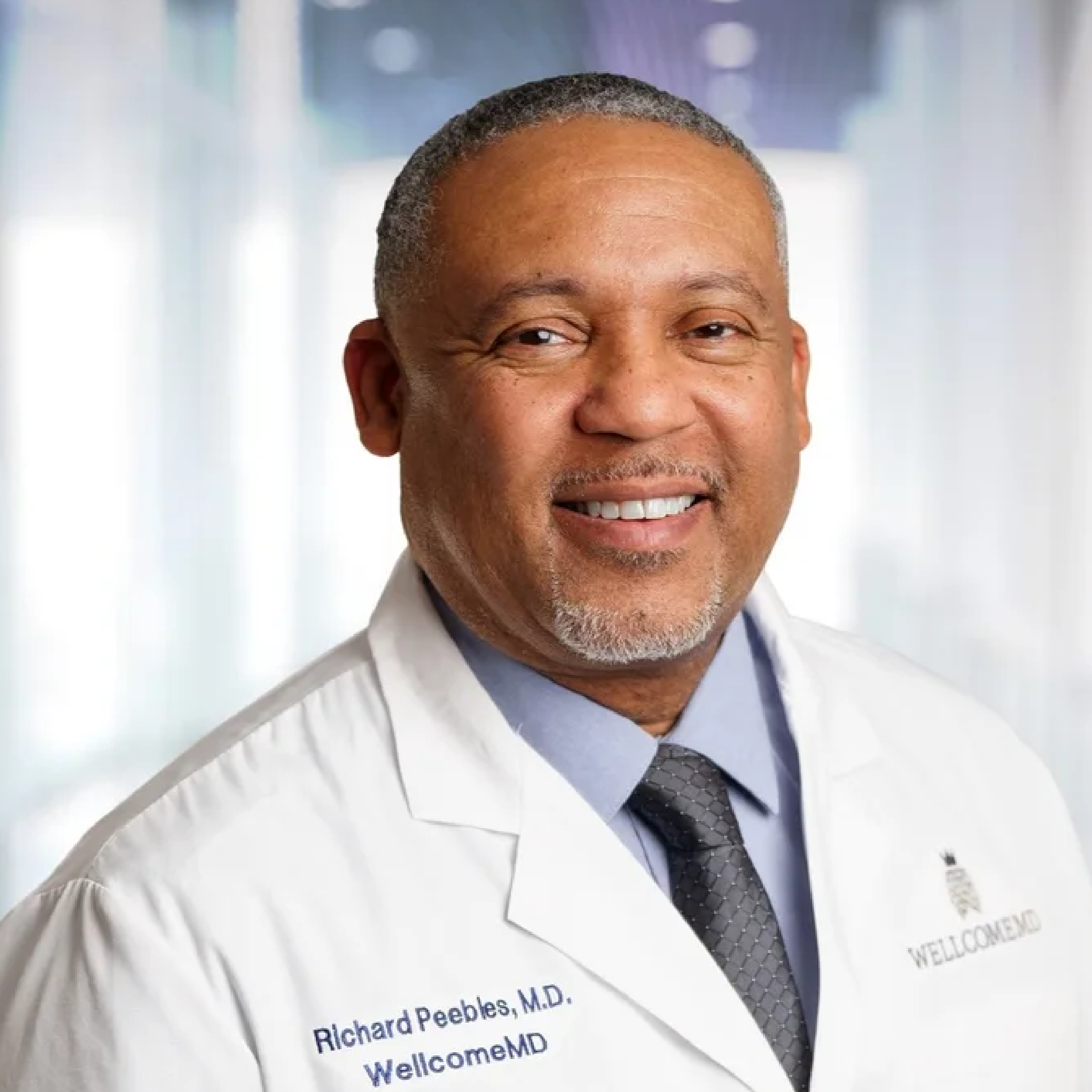 Smiling doctor in a white coat with a name badge reading Richard Peebles, M.D., at a welcome event.