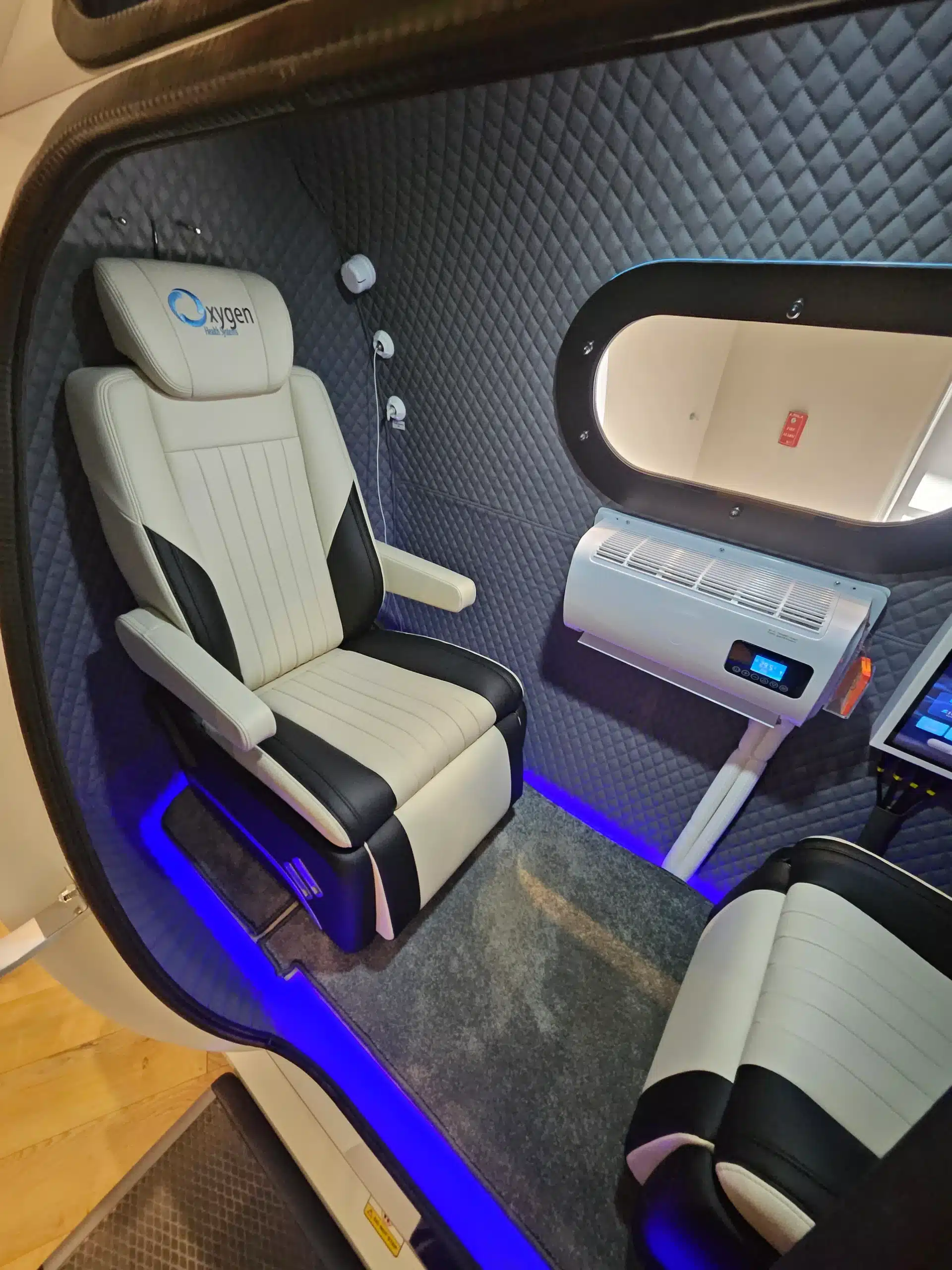 HBOT Section 2 - WellcomeMD Quilted blue interior of a pod-style vehicle with cream leather seat, window, and blue LED floor lighting