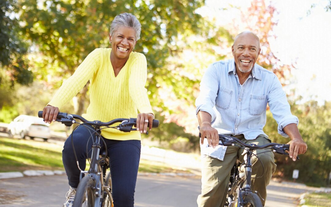 Two adults riding bikes together outdoors, smiling and enjoying a sunny park day.